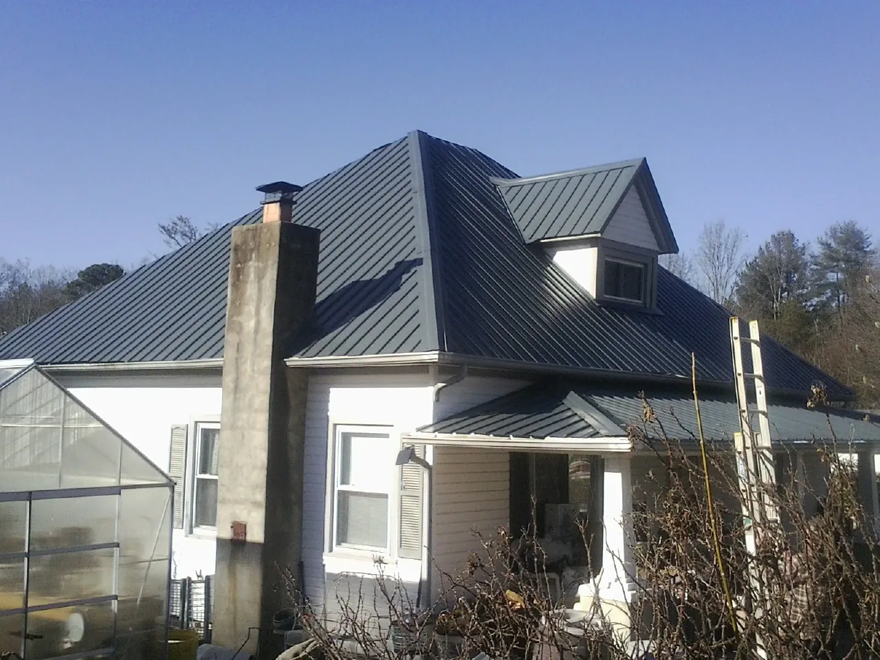 Dark blue standing seam metal roof on a white farmhouse with dormer — Slate & Tile Roof Repair by Roofing Brothers in Wendell