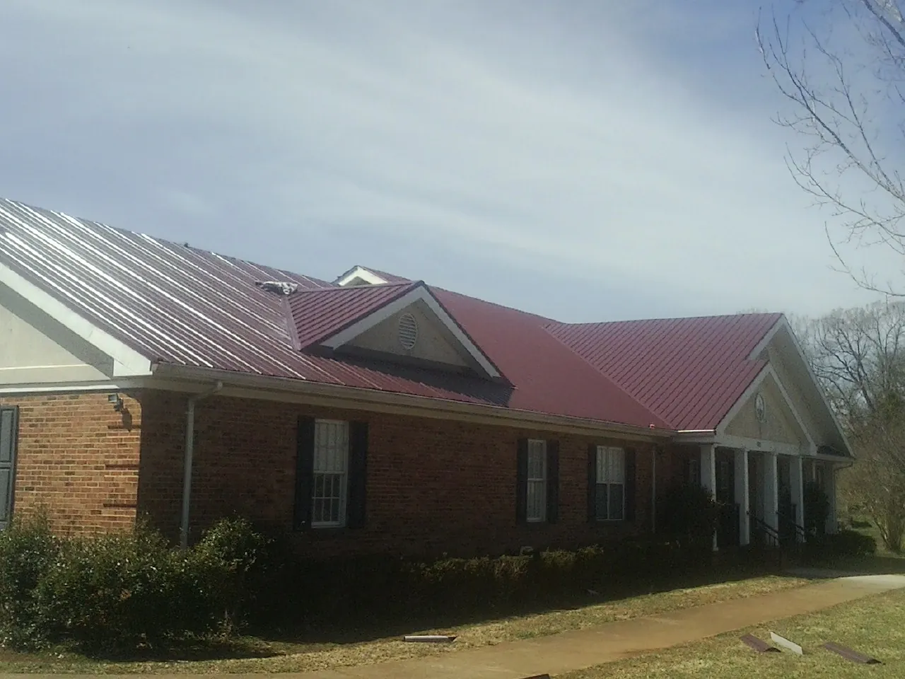 Red metal roof with gabled entries on a long brick building, from a Hail Damage Roof Repair job in Wendell