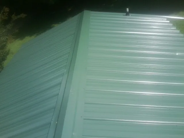 New green metal panels meeting at the ridge of a roof — Flat Roof Repair work by our crew in Wendell