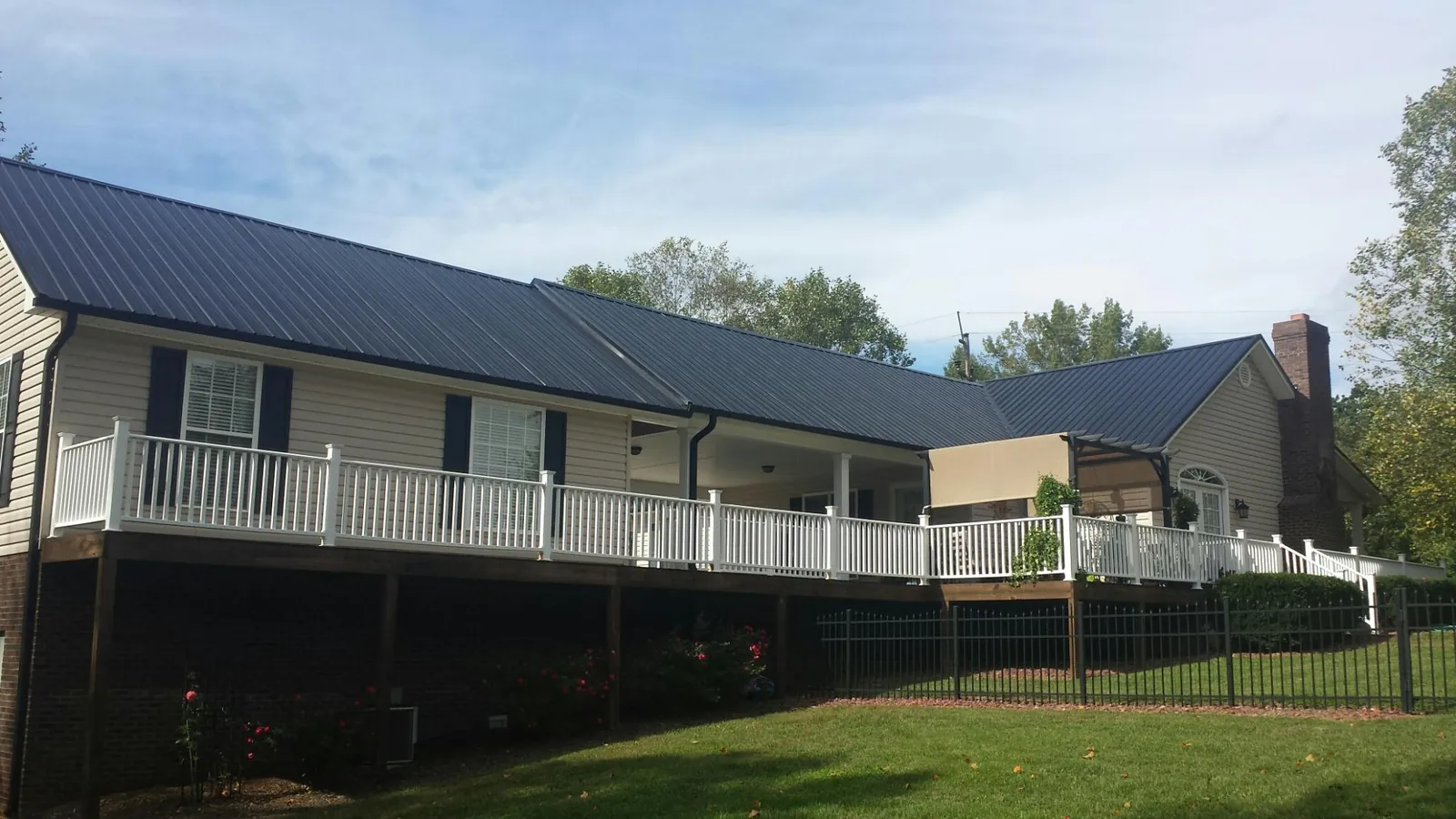 Black metal roof above a long white railed deck on a hillside home in Wendell
