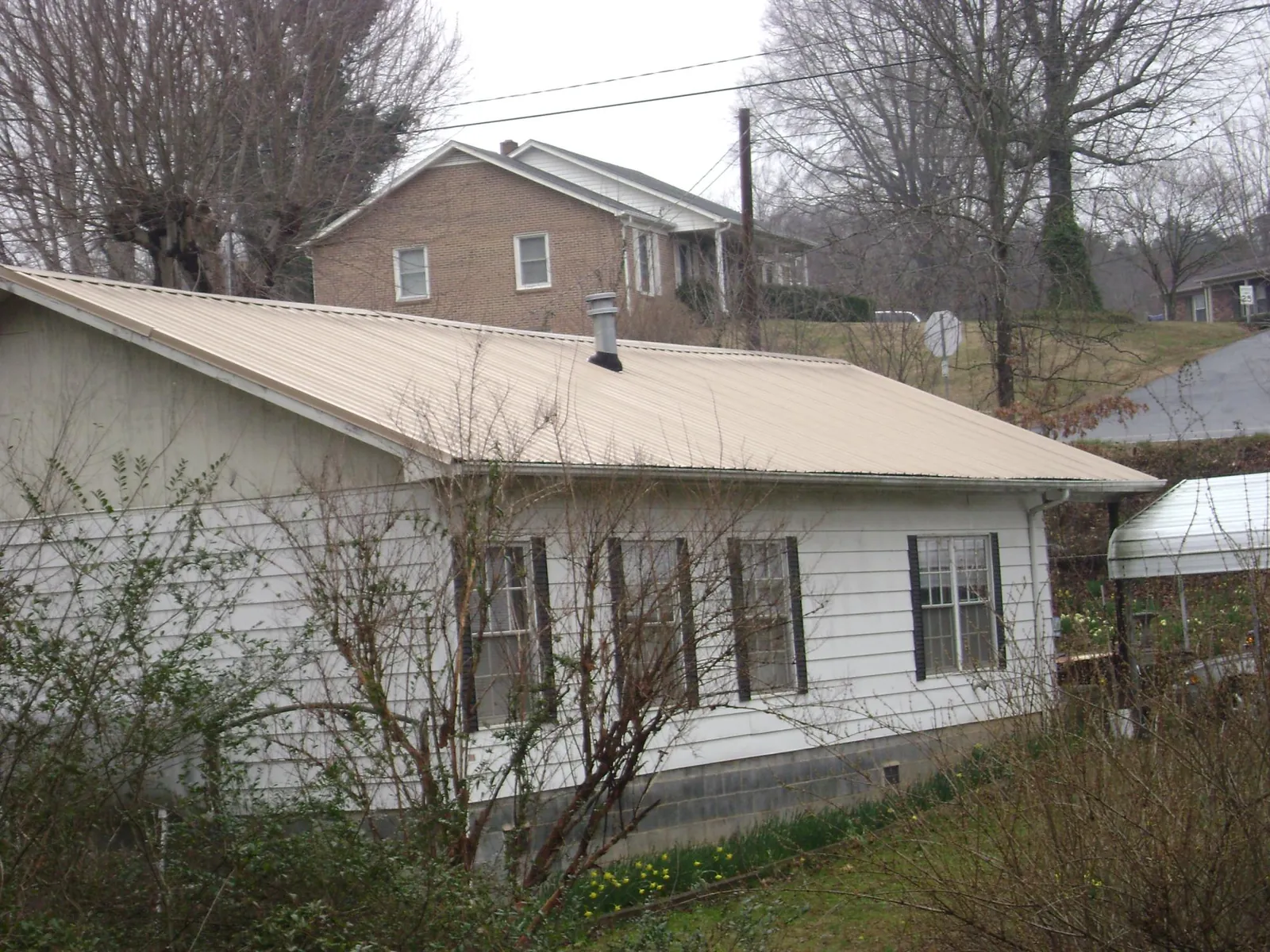 Tan metal roof on a white sided house set into a hillside — Commercial Roofing by Roofing Brothers in Wendell
